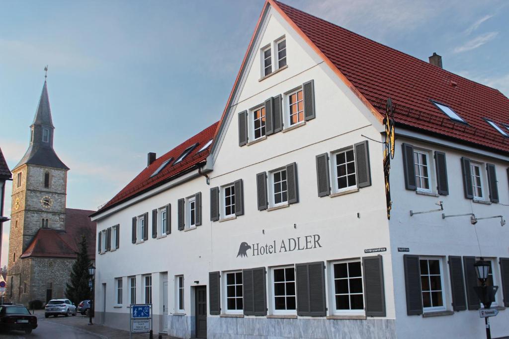 a white building with a red roof and a church at Hotel Adler in Bad Friedrichshall
