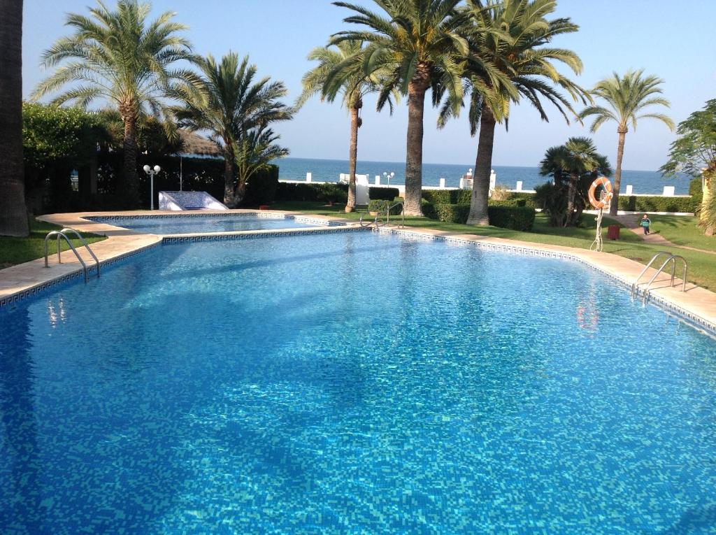 a large swimming pool with palm trees and the ocean at Urbanizacion primera línea de playa in Denia