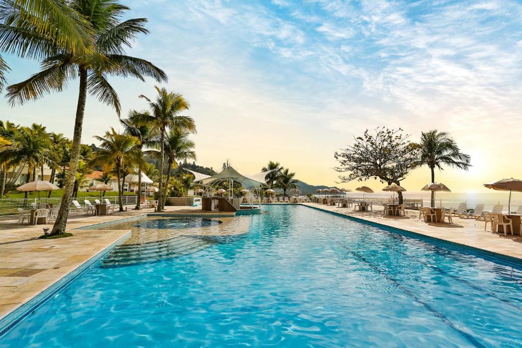 una piscina en un complejo con palmeras y el océano en Itapema Beach Hotéis by Nobile en Itapema