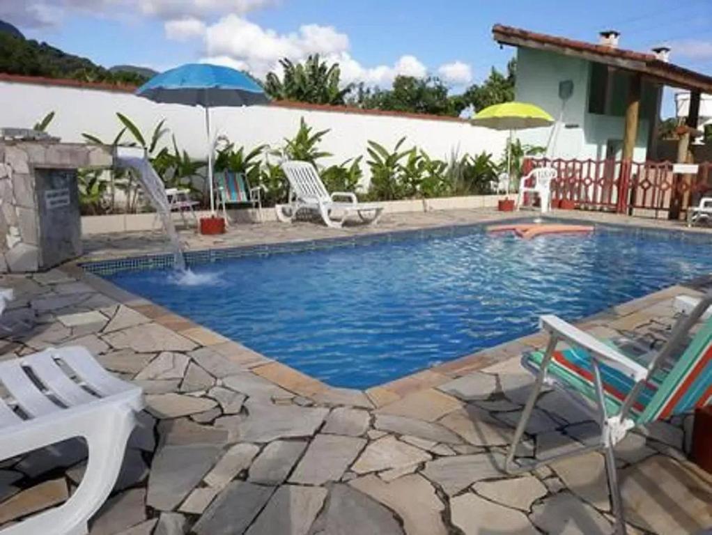 uma piscina com cadeiras e um guarda-sol em POUSADA TANI COM PISCINA em MARESIAS em Maresias