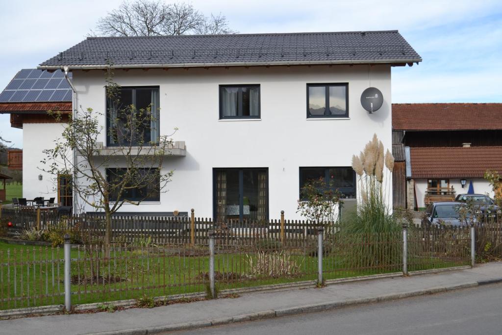 une maison blanche avec un toit noir et une clôture dans l'établissement Alpenblick Ferienwohnung, à Bad Feilnbach