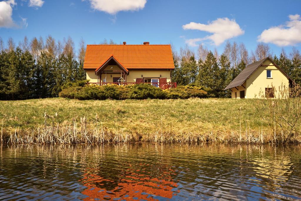 a house with an orange roof next to a body of water at Leśniczówka Niebrzydowo in Morąg