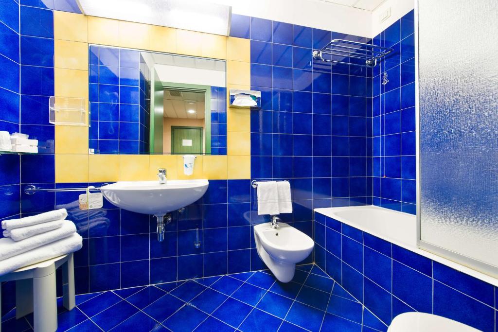 W wyłożonej niebieskimi kafelkami łazience znajduje się umywalka i toaleta. w obiekcie Best Western Hotel Mediterraneo w Katanii