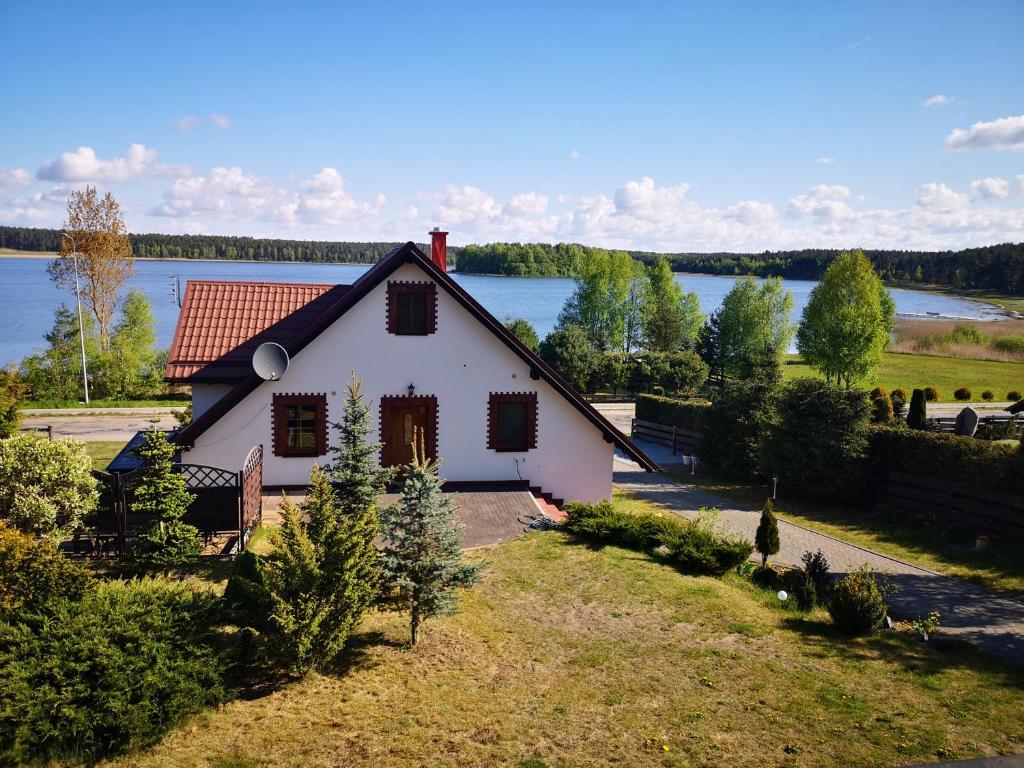 une petite maison blanche avec un lac en arrière-plan dans l'établissement Agroturystyka Dobri mól, à Kiedrowice