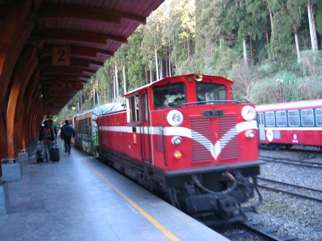 un tren rojo está llegando a una estación de tren en 登山別館, en Zhongzheng