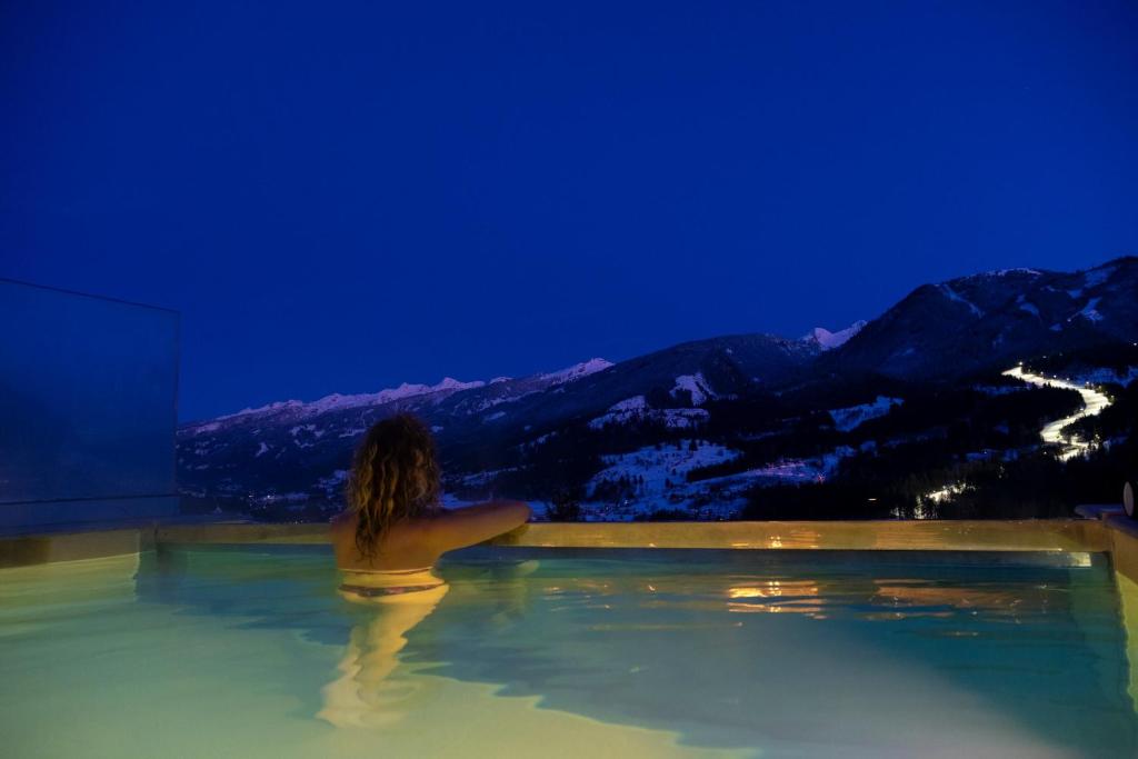 Una donna in una vasca idromassaggio che guarda le montagne di La Roccia Wellness Hotel a Cavalese