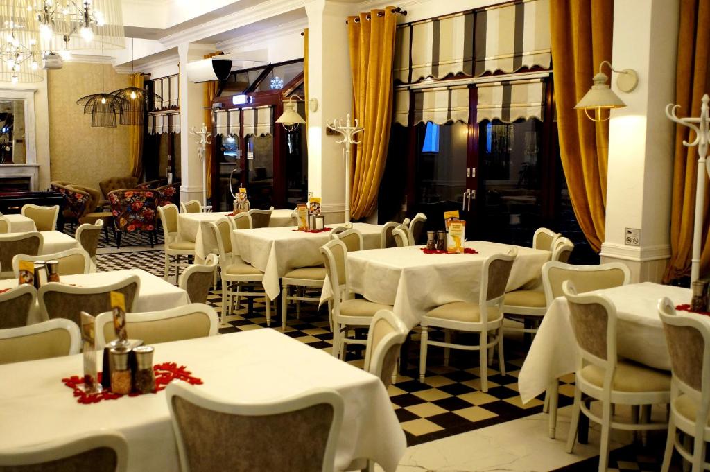 Elegant dining room with white-clothed tables, black-and-white checkered floor, yellow curtains and warm lighting.