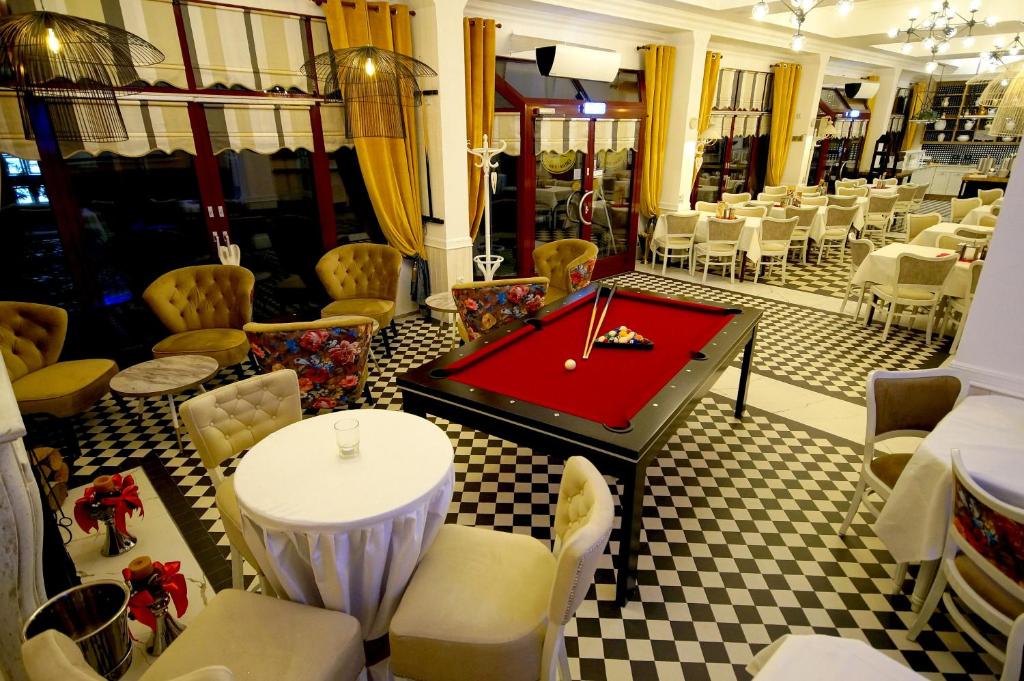 Spacious dining-lounge with central pool table, checkered flooring, yellow curtains and multiple dining setups.