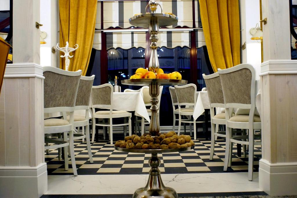Three-tier metal fruit stand centered on checkered-floor dining room with white chairs and mustard curtains.