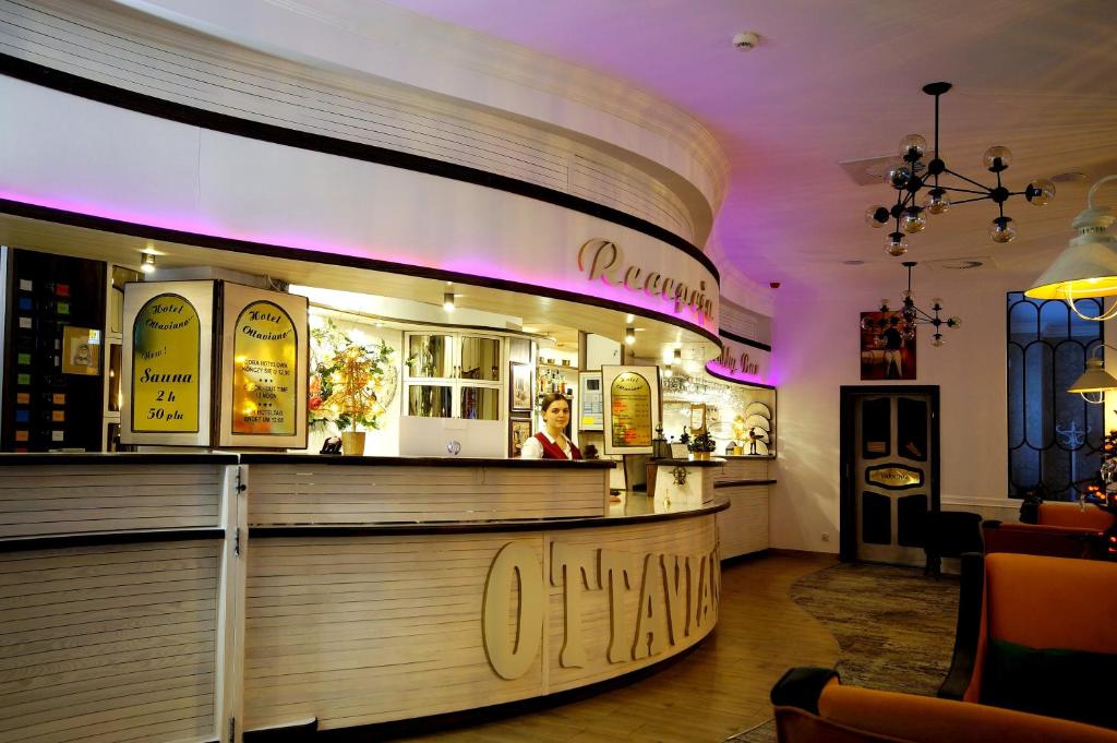 Wide reception area with smiling receptionist, chandeliers, curved wooden desk and ambient purple glow.