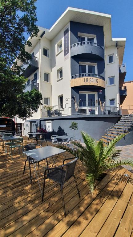 a building with tables and chairs on a wooden deck at Hôtel La Baïne in Capbreton