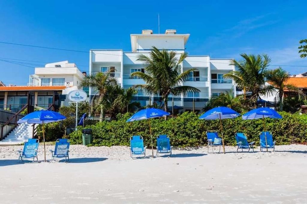 un grupo de sillas y sombrillas azules en una playa en Bombinhas Blue Suítes, en Bombinhas
