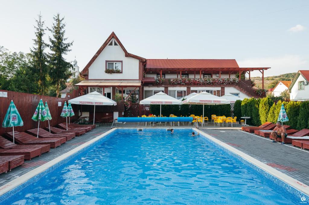 a pool with chairs and umbrellas in front of a building at Pensiunea Nemes Panzio in Acăţari