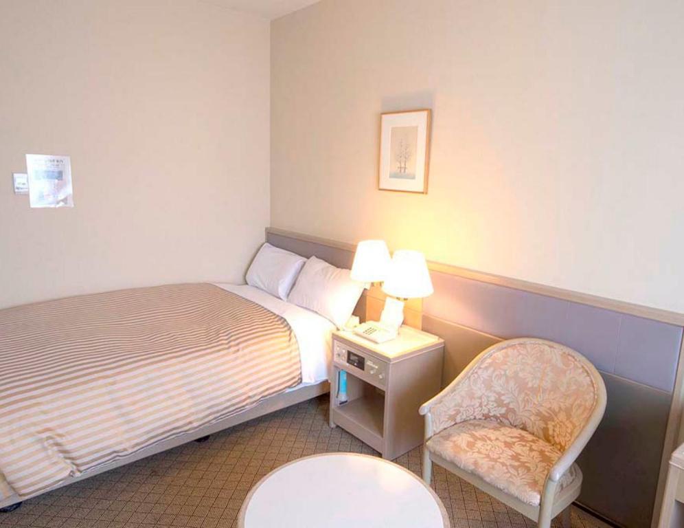 um quarto de hotel com uma cama e uma cadeira em Grand Hotel Kanachu Hadano em Hadano