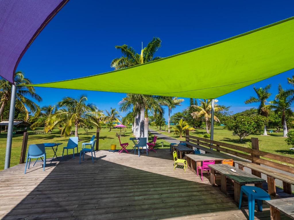 a deck with tables and chairs under a green umbrella at Auberge de Poé in Bourail