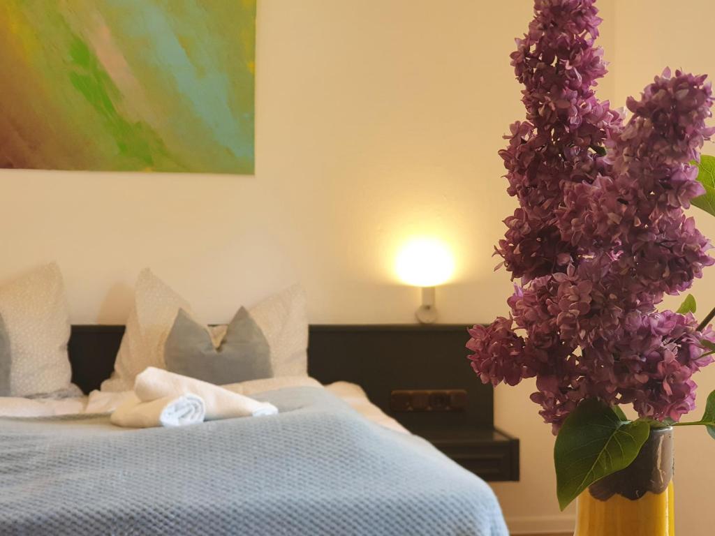 ein Schlafzimmer mit einem Bett mit einer Vase lila Blumen in der Unterkunft Garni Hotel Biebertal am Milseburgradweg in Hofbieber