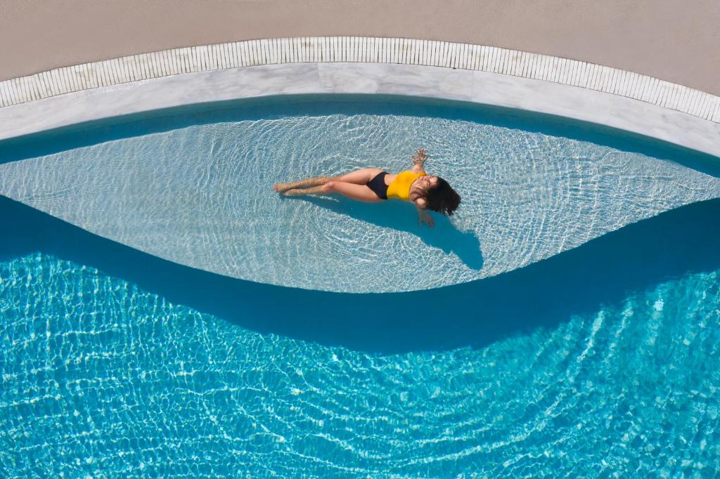 a man swimming in a pool on a blue surfboard at Lilium Hotel Santorini in Fira
