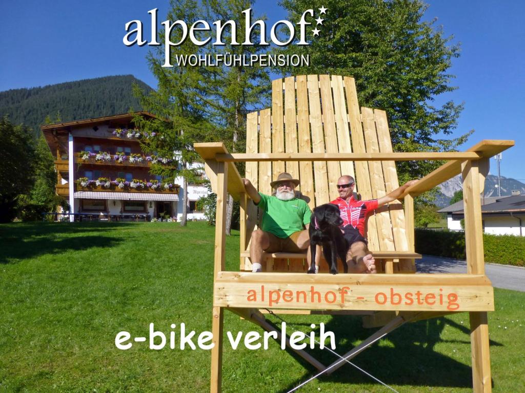 Zwei Männer und ein Hund sitzen auf einem großen Stuhl. in der Unterkunft Alpenhof Wohlfühlpension in Obsteig