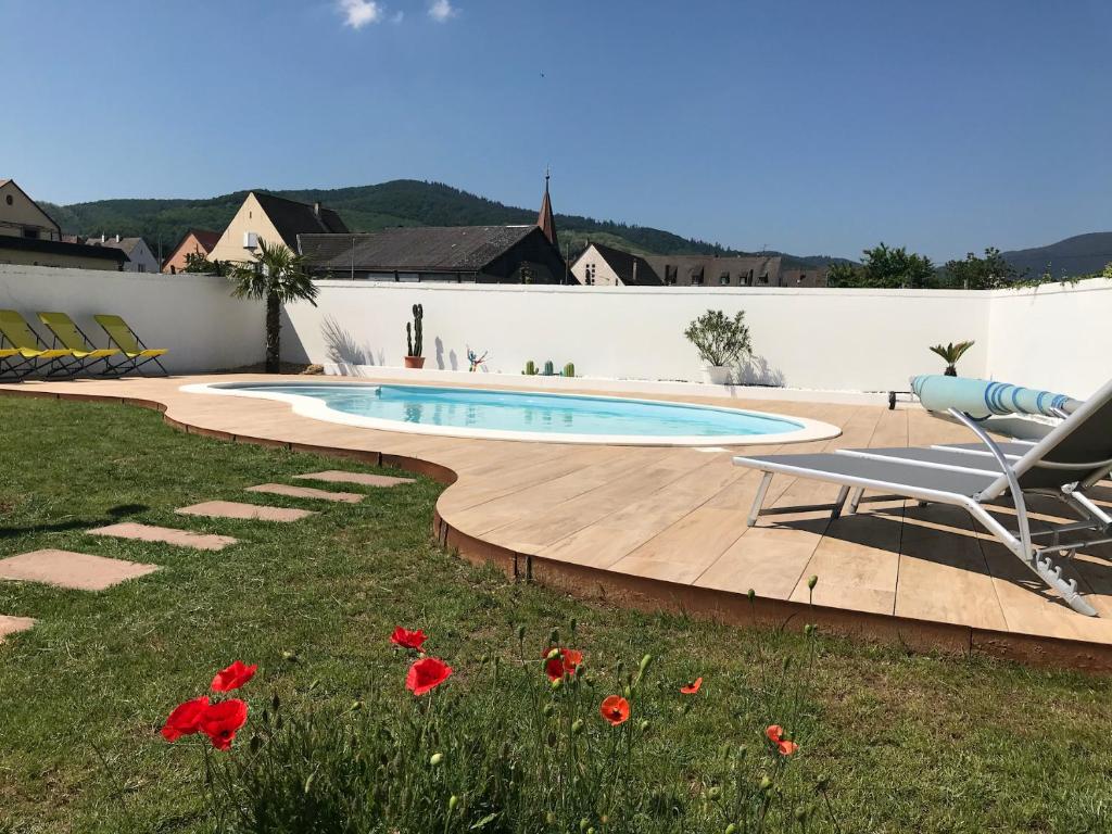 uma piscina num quintal com uma cadeira e flores em Alsacebnb - Gîte 12 personnes dans le vignoble - Piscine privée chauffée & Spa em Ammerschwihr