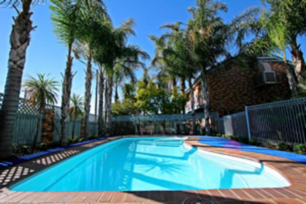 a swimming pool in front of a house with palm trees at Cattlemans Country Motor Inn & Serviced Apartments in Dubbo