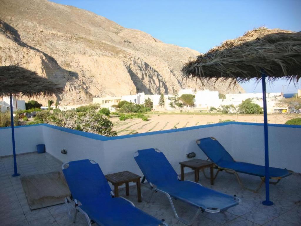 un patio con sillas y sombrillas azules y una montaña en Studios Halaris, en Perissa