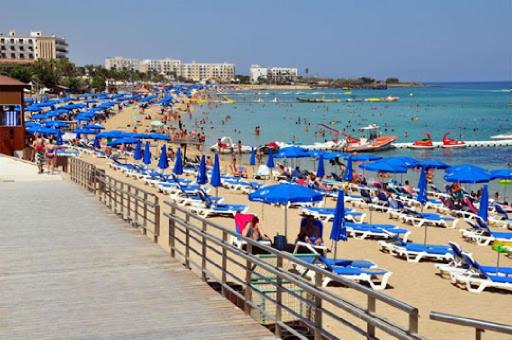 una playa llena de gente con sombrillas azules y gente en ella en Georgianno Sea Apartments, en Protaras