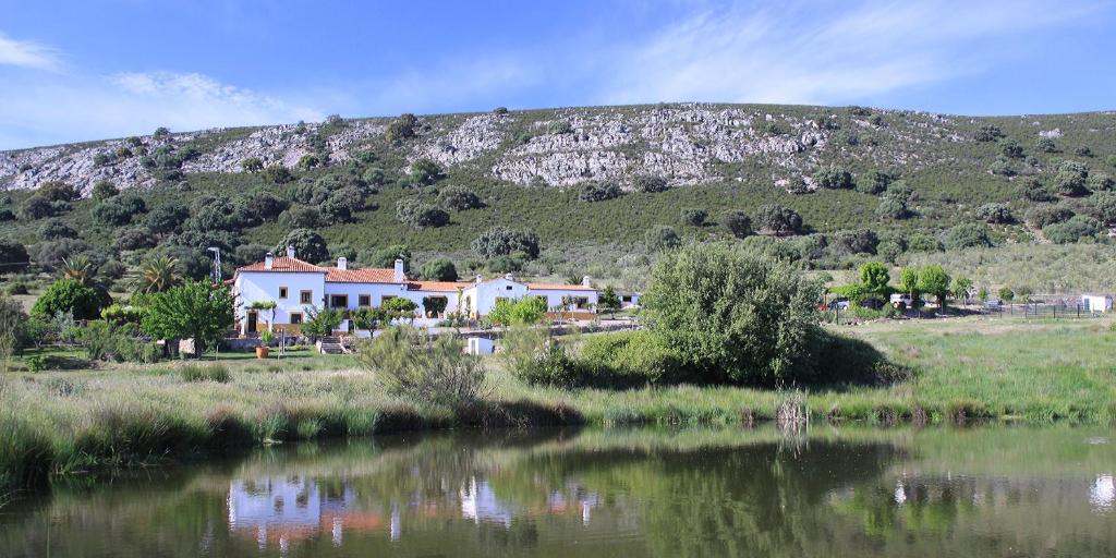 una casa en una colina junto a un cuerpo de agua en Palacio Viejo de Las Corchuelas en Torrejón el Rubio