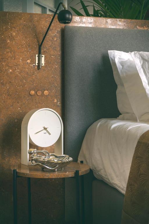 a clock on a table next to a bed at Aristide Hotel - Small Luxury Hotels of the World in Ermoupoli