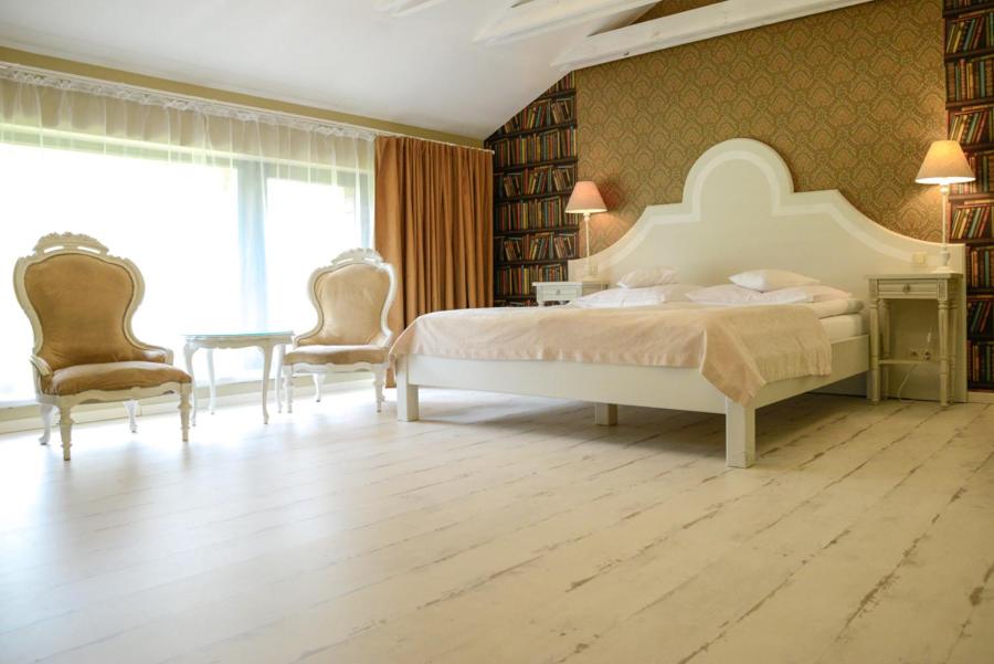 Elegant bedroom with large bed, vintage chairs, and bookshelf wallpaper.