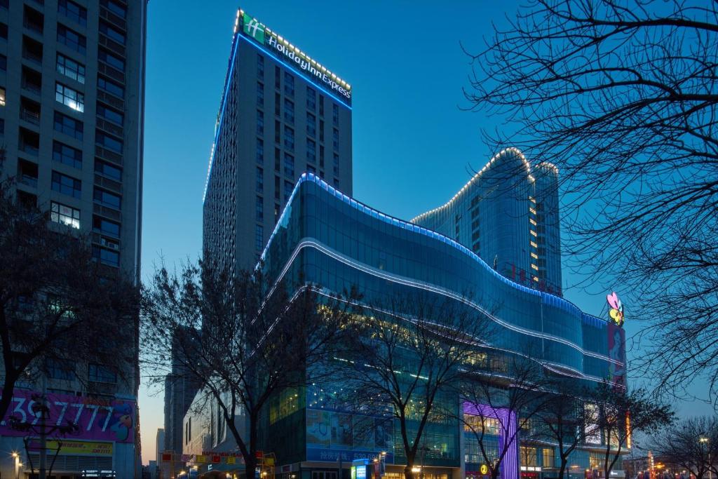 twee hoge gebouwen in een stad 's nachts bij Holiday Inn Express Tangshan Downtown, an IHG Hotel in Tangshan