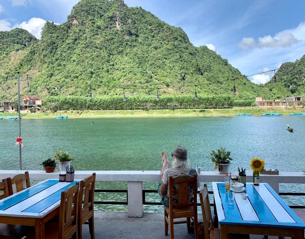 une femme assise à une table donnant sur l'eau dans l'établissement Funny Monkeys Homestay, à Phong Nha