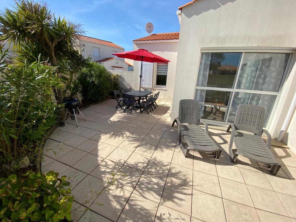 un patio con sillas y una mesa con una sombrilla roja en Maison de vacance proche de la mer en Les Sables-dʼOlonne