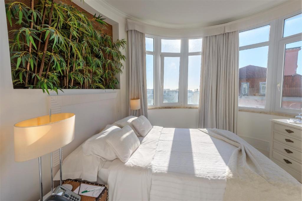 a white bedroom with a bed and a large window at Amazonia Estoril Hotel in Estoril