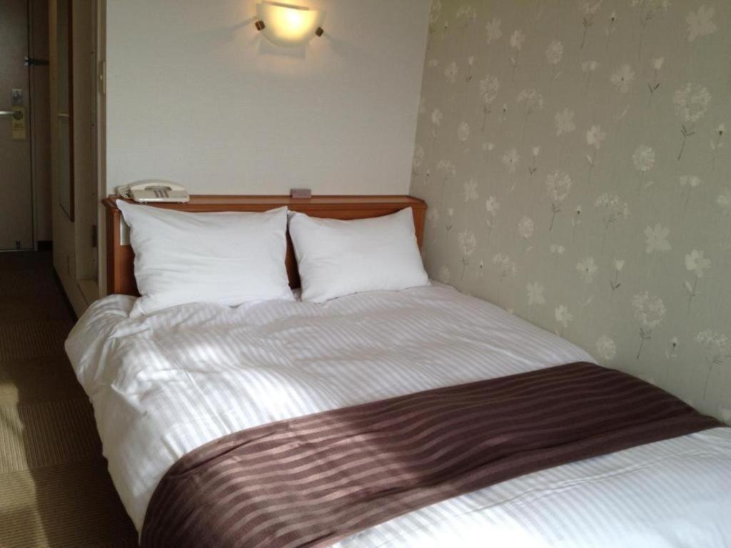 Bett mit weißer Bettwäsche und Kissen in einem Zimmer in der Unterkunft Tottori City Hotel / Vacation STAY 81358 in Tottori