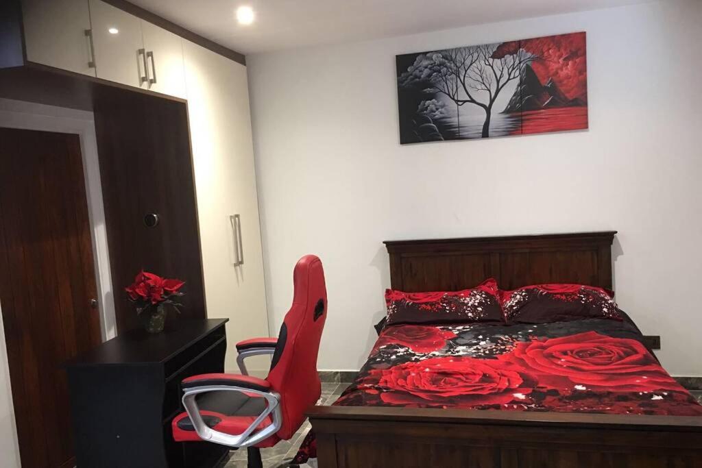 Schlafzimmer mit einem Bett mit roter Bettwäsche und einem Stuhl in der Unterkunft Bright, stylish Studio flat with Sky Sports in Earley