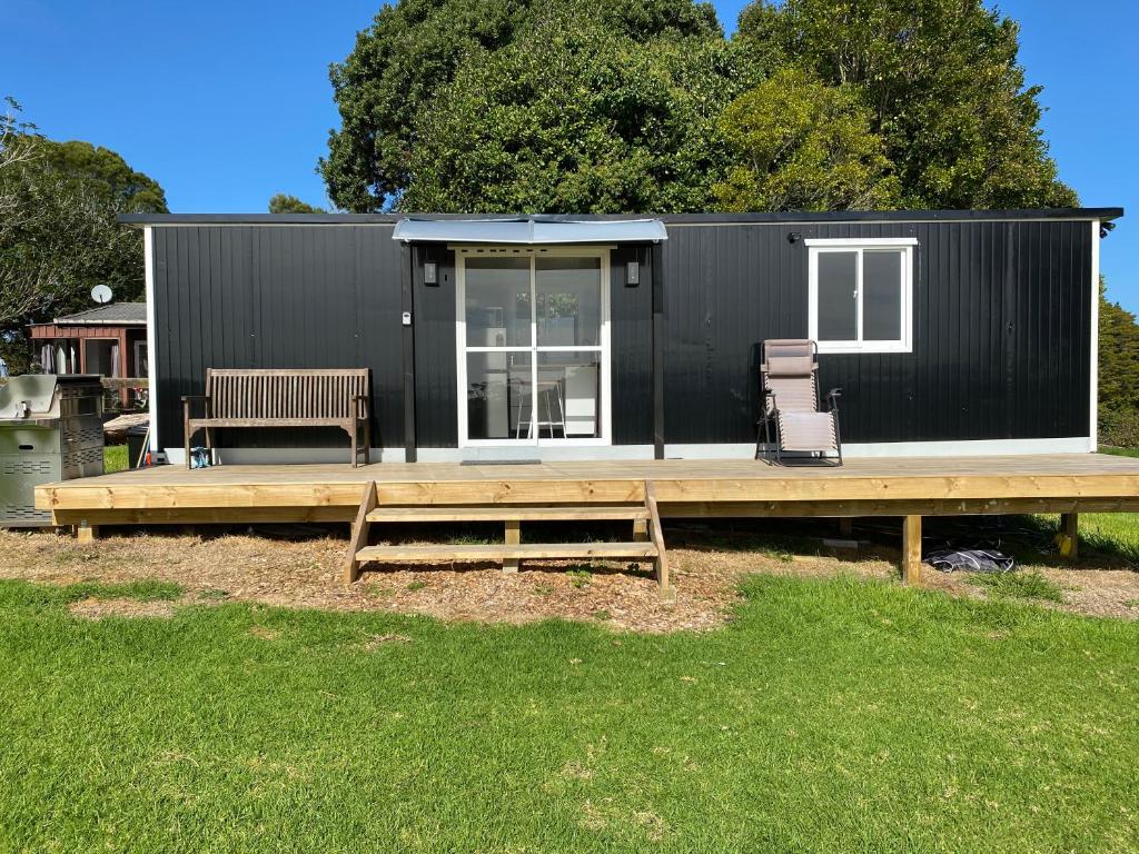 ein schwarzes winziges Haus mit einer Terrasse und einer Bank in der Unterkunft Cosy cabin to stay even better than Glamping in Pukekohe East
