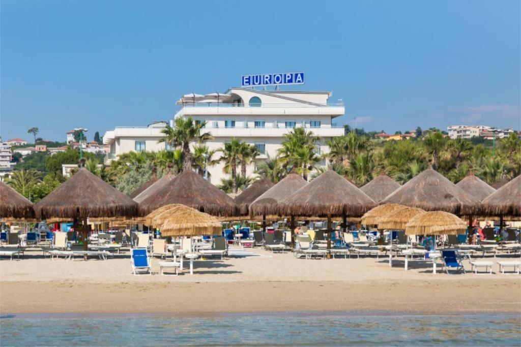 una spiaggia con ombrelloni e sedie di paglia e tavoli di Hotel Europa Beach Village a Giulianova