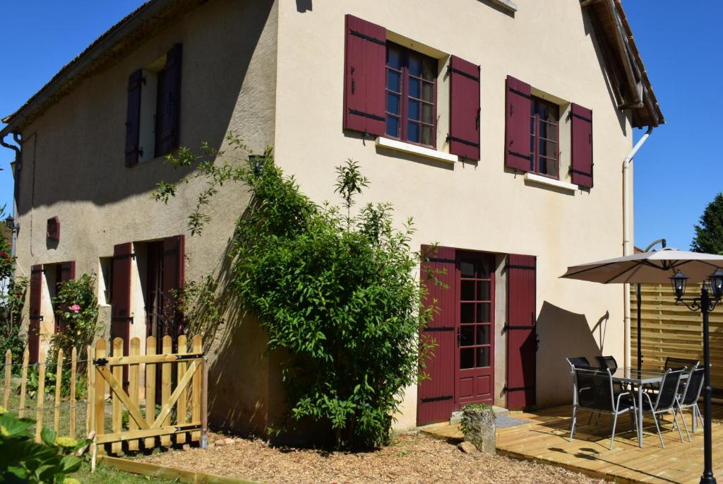 ein Haus mit roten Rollläden, einem Tisch und einem Regenschirm in der Unterkunft LOU CLEDOU in Cendrieux