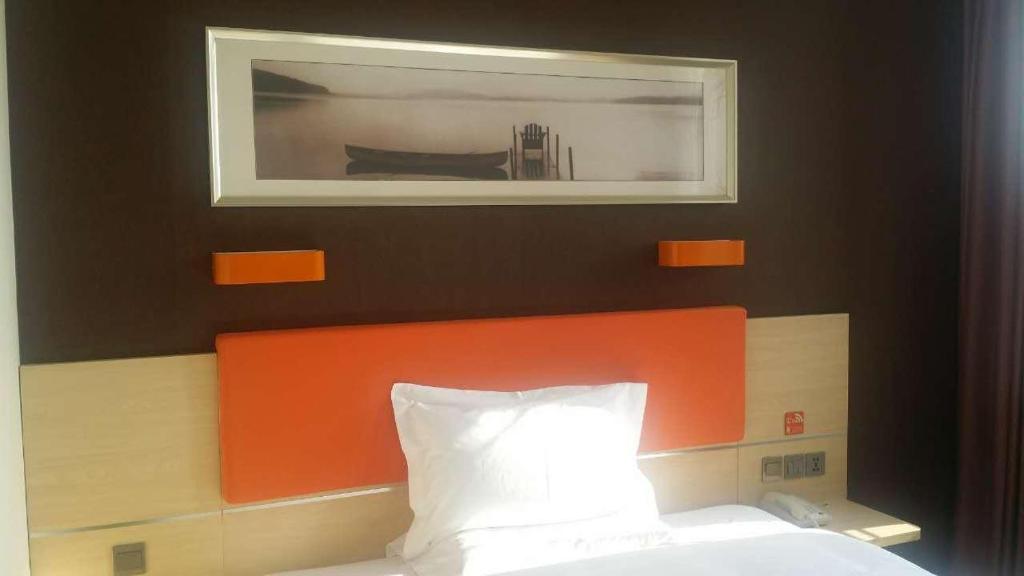 a bed with an orange headboard and a picture above it at 7Days Premium Zhangjiakou Xuanhua Bell Tower High Speed Railway Station Branch in Zhangjiakou