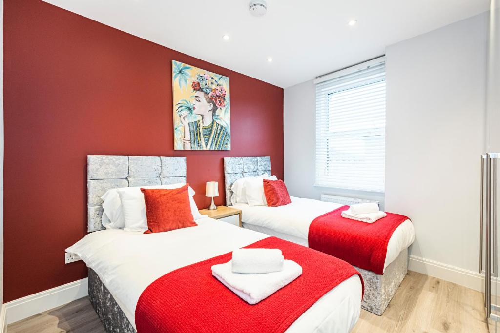 2 Betten in einem Zimmer mit roten Wänden in der Unterkunft Cozy and Serene brand-new flat in Kilburn, London in London