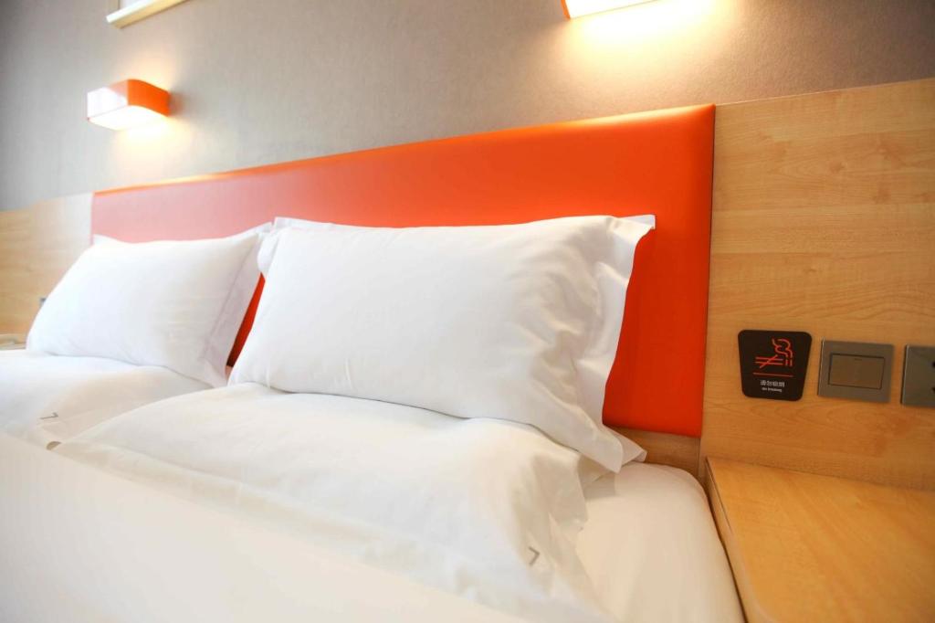 un letto con testiera arancione e cuscini bianchi di 7Days Premium Zhengzhou Songshan Road Rose Park Subway Station Branch a Zhengzhou