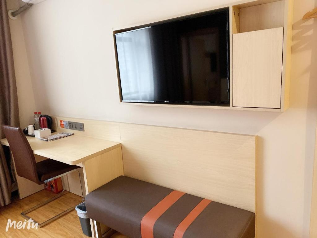 Habitación pequeña con escritorio y TV en la pared. en 7Days Premium Shenyang Olympic Sports Center Subway Station Branch, en Shenyang