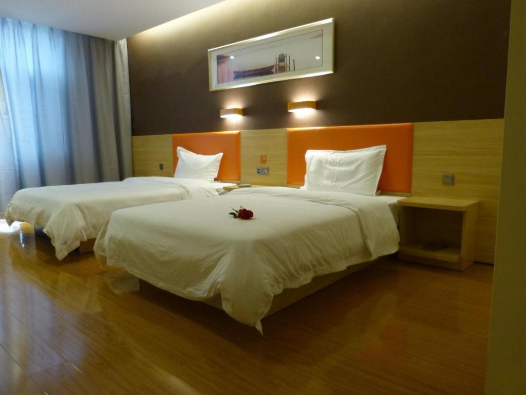 two beds in a hotel room with a flower on them at 7Days Premium Delingha Center Plaza Branch in Delingha