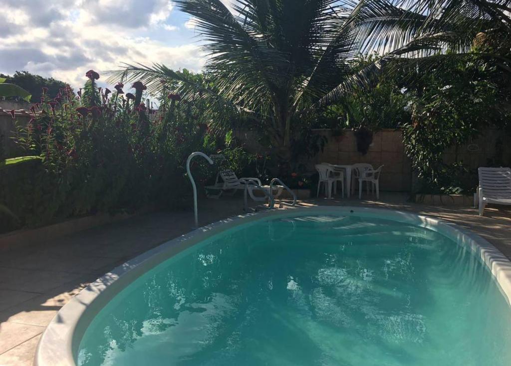 einen Pool in einem Garten mit Stühlen und einer Palme in der Unterkunft Suíte 10 com wifi a 4 min da praia em Caraguá in Caraguatatuba