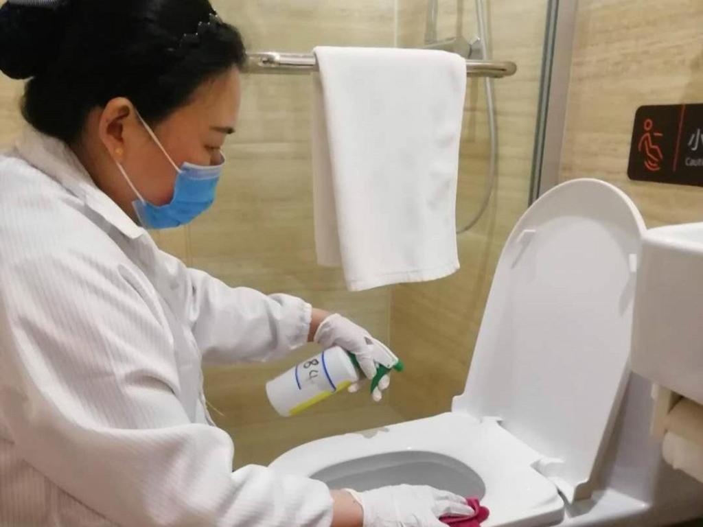 a woman in a mask and gloves cleaning a toilet at 7Days Premium Luoyang Peony Park Shanghai Market Branch in Luoyang