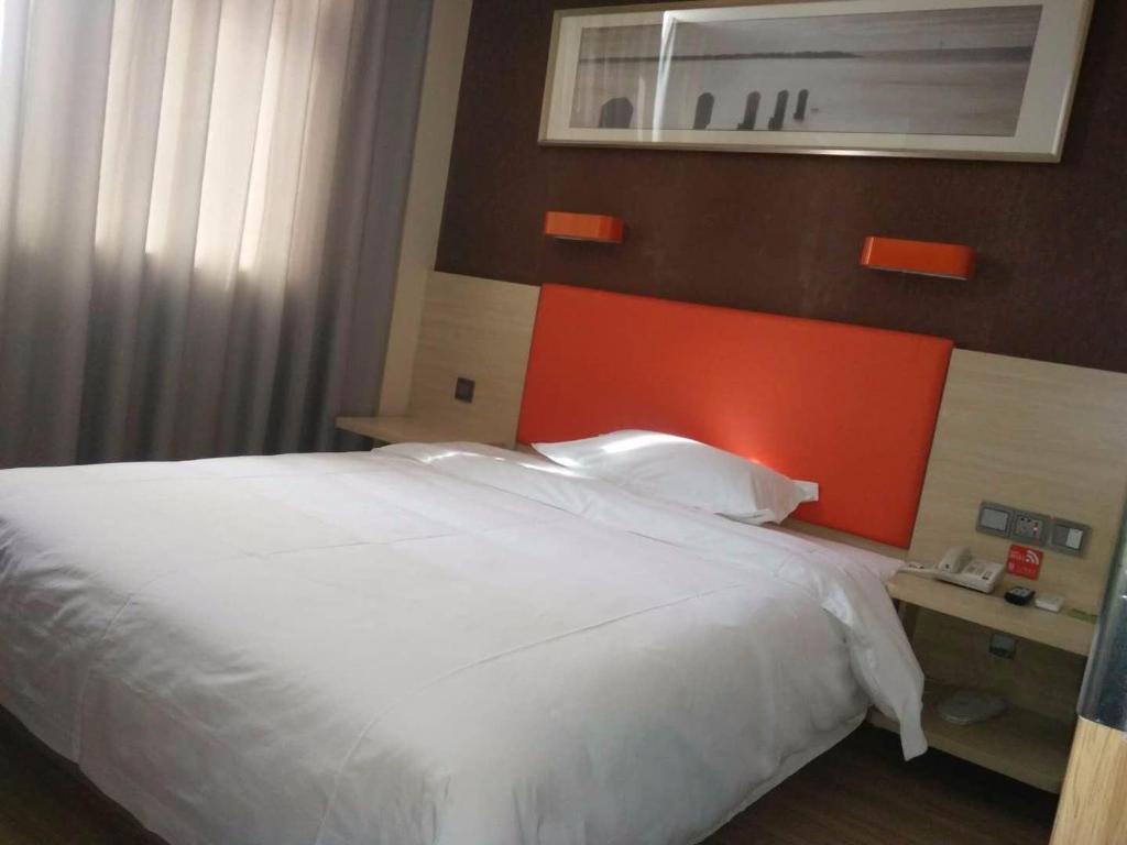 a bedroom with a white bed with an orange headboard at 7Days Premium Dingxi Train Station Branch in Dingxi