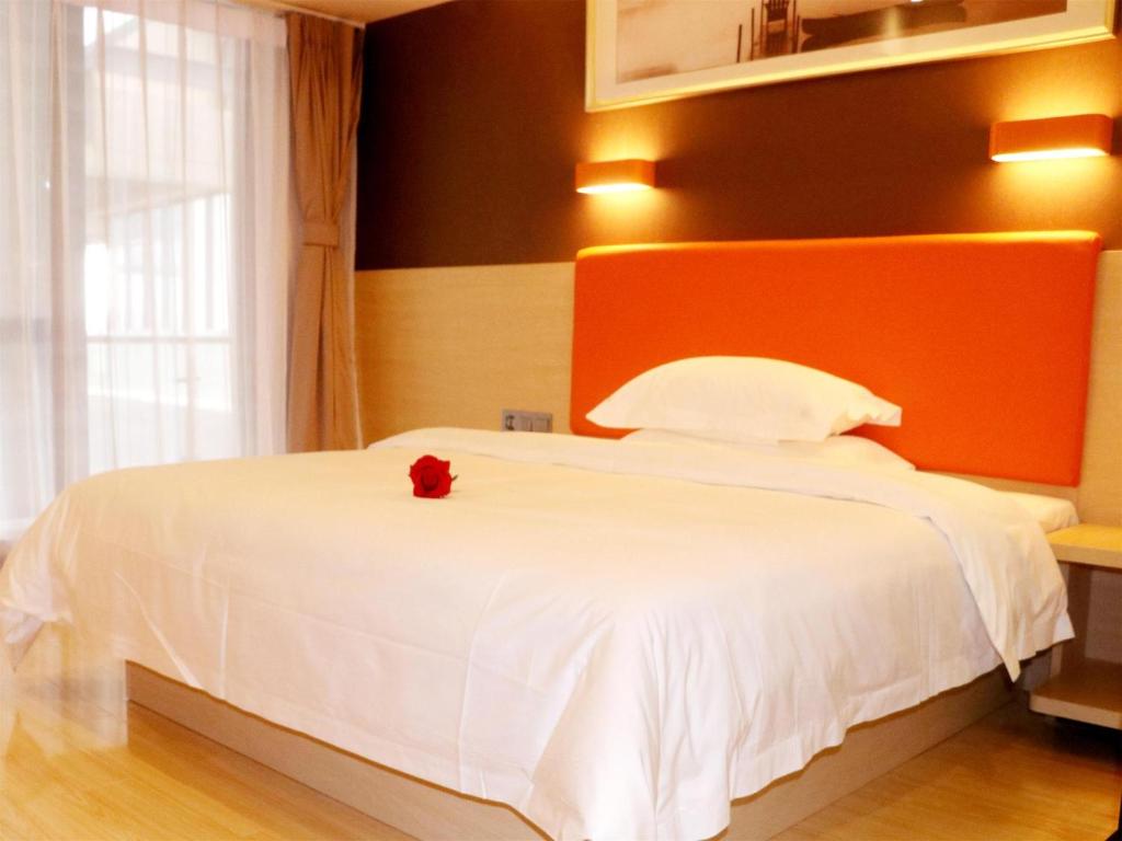 Un dormitorio con una cama blanca con una flor roja. en 7Days Premium Jinan West Railway Station Branch en Jinan