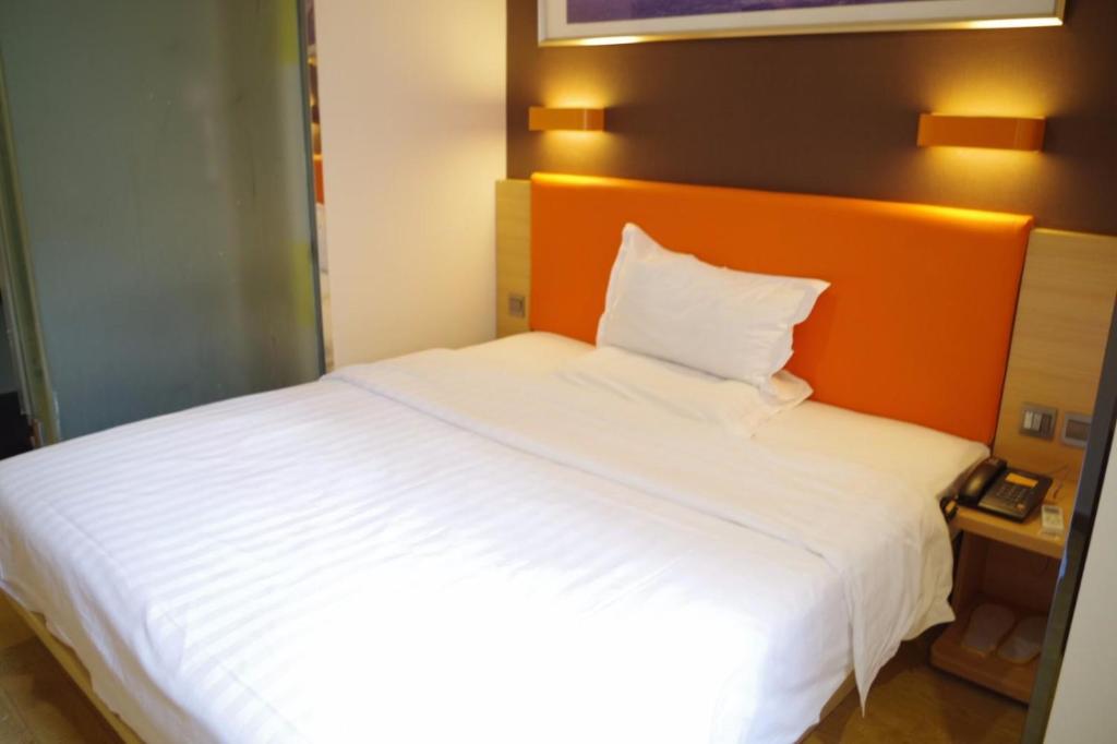 7Days Premium Hefei Mingguang Road Bus Station Branch في خفي: غرفة نوم مع سرير أبيض مع اللوح الأمامي من البرتقال