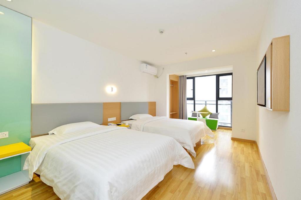 2 Betten in einem Schlafzimmer mit weißen Wänden und Holzböden in der Unterkunft 7Days Inn Nanchang West Station Huanan Cheng Wangcheng New District Branch in Nanchang