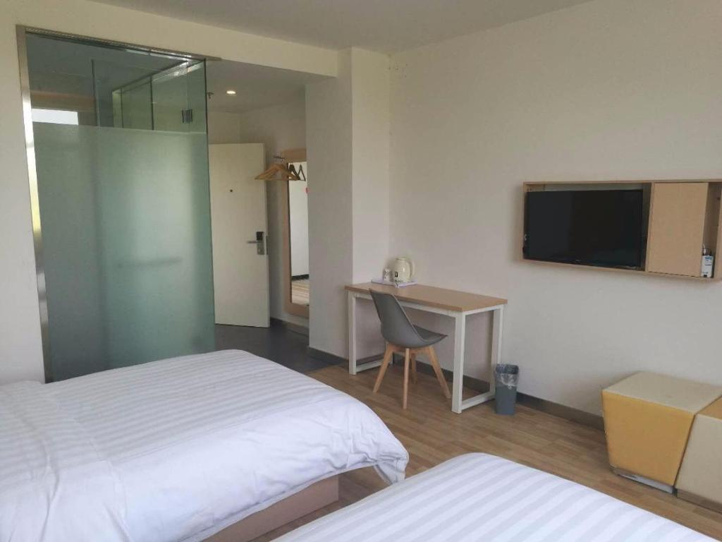 a room with two beds and a desk and a television at 7Days Inn Chizhou Jiuhuashan Branch in Chizhou